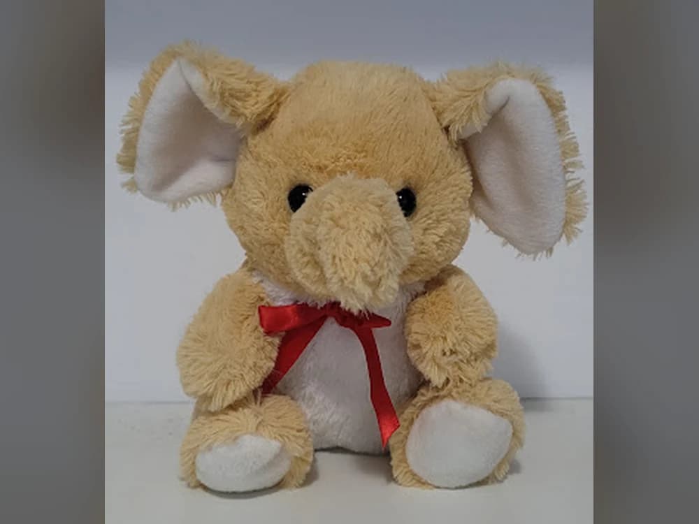 Um bichinho de pelúcia de elefante bege, com laço vermelho no pescoço, sentado.
